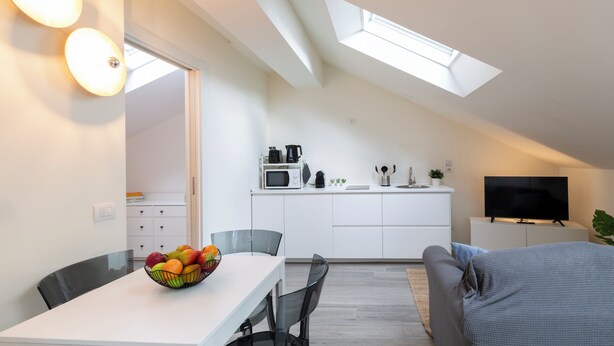 A modern apartment with a dining area, kitchenette, and a living space with a TV and sofa. - notaMi - Bright Attic M4 - 2 Bedrooms (Milan)