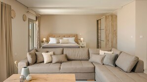 A modern bedroom with a large beige sectional sofa, a wooden coffee table, and a bed with a wooden headboard. - Villa Armonia - Zen Villas (Fiskardo)