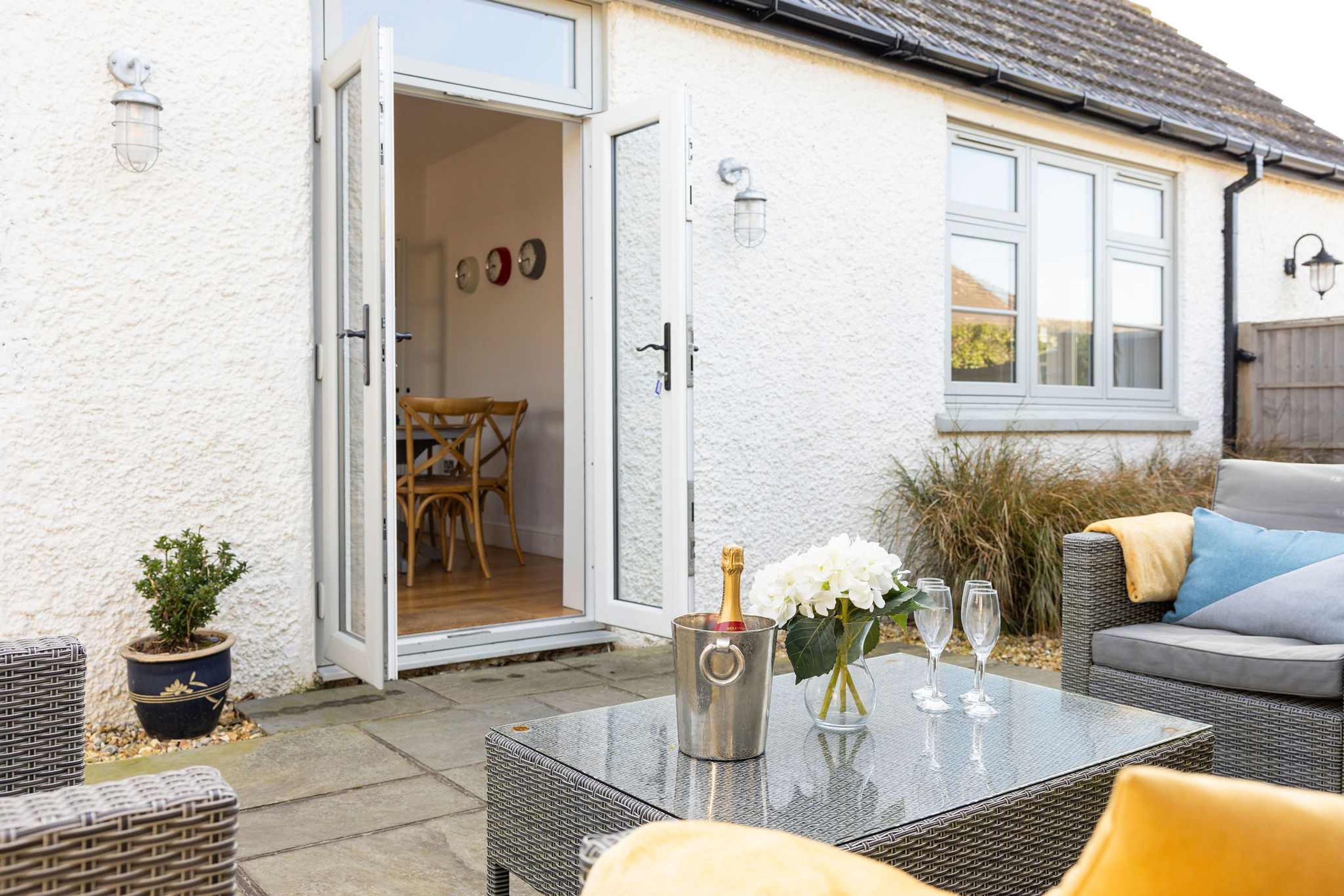 An open door leading to a dining area with a table set for two, a potted plant, and a wicker chair.