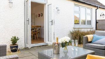 An open door leading to a dining area with a table set for two, a potted plant, and a wicker chair.