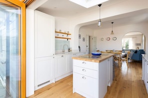 A modern kitchen with white cabinetry, a wooden countertop, and a skylight. - Charming Seaside Cottage - 5-min Walk to Beach (Chichester)