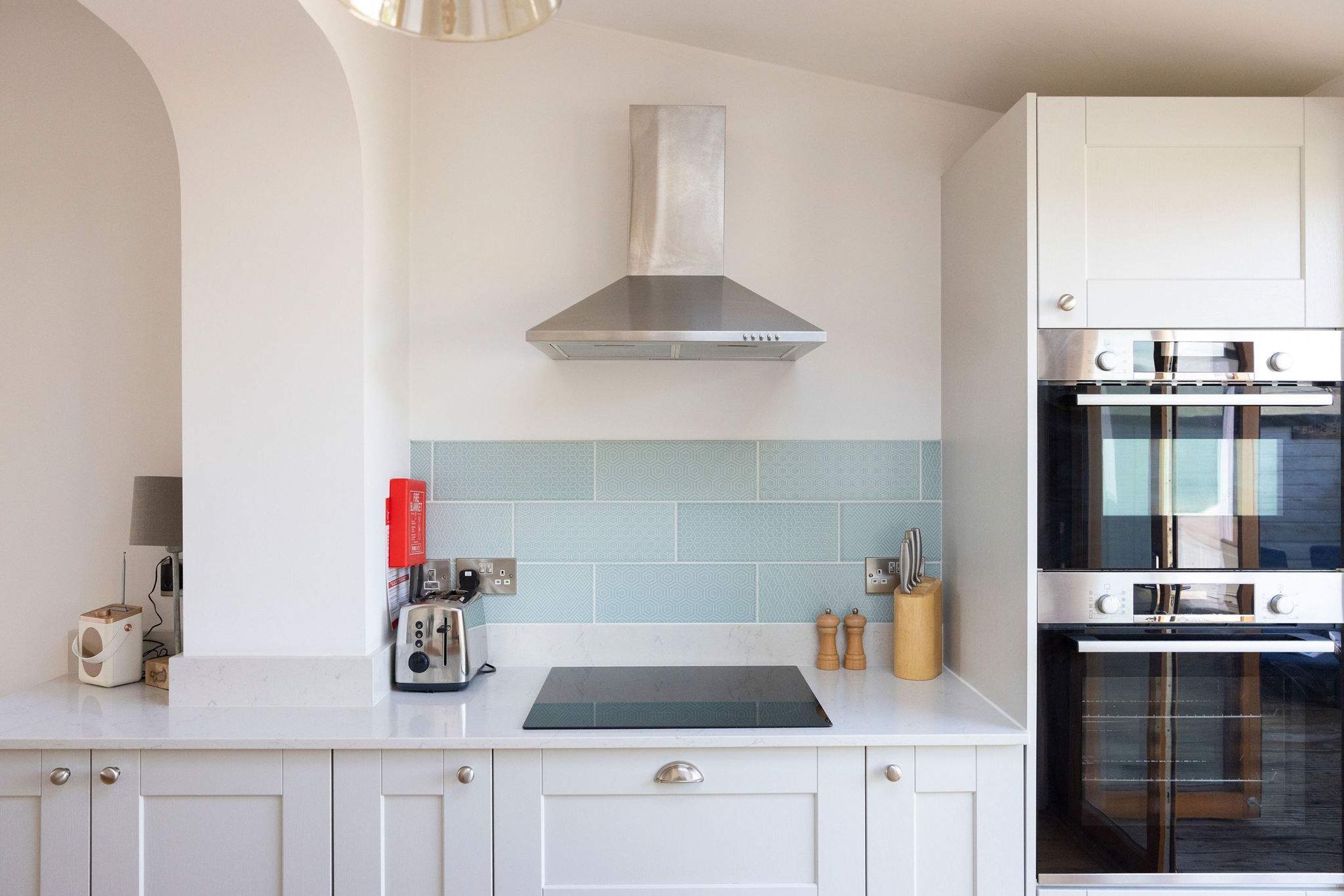 Een moderne keuken met witte kasten, een roestvrijstalen afzuigkap, een dubbele oven en een betegelde spatwand.