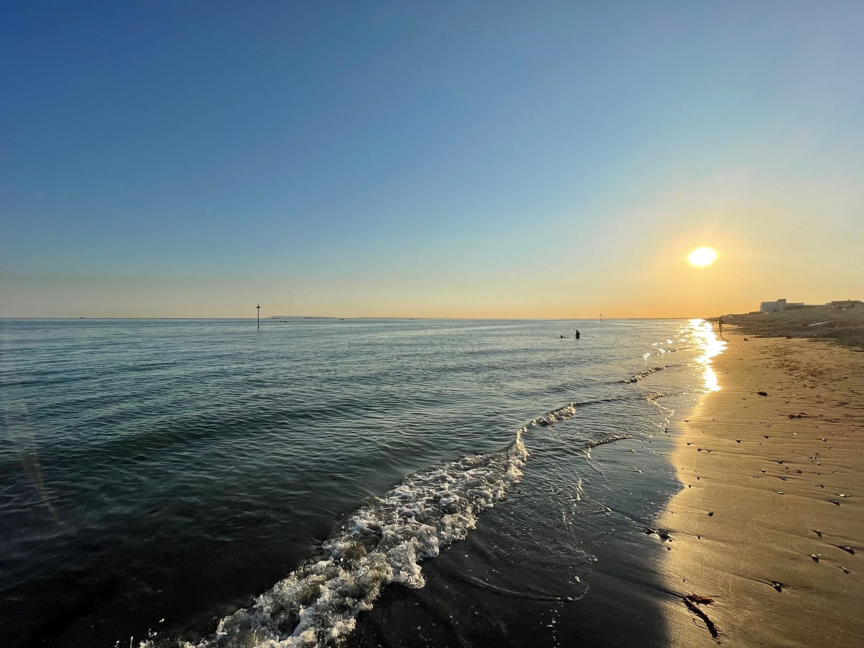 A beach with a clear sky and the sun setting on the horizon.