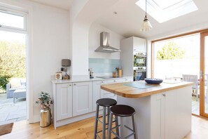 A modern kitchen with white cabinets, a wooden island, and a skylight. - Charming Seaside Cottage - 5-min Walk to Beach (Chichester)