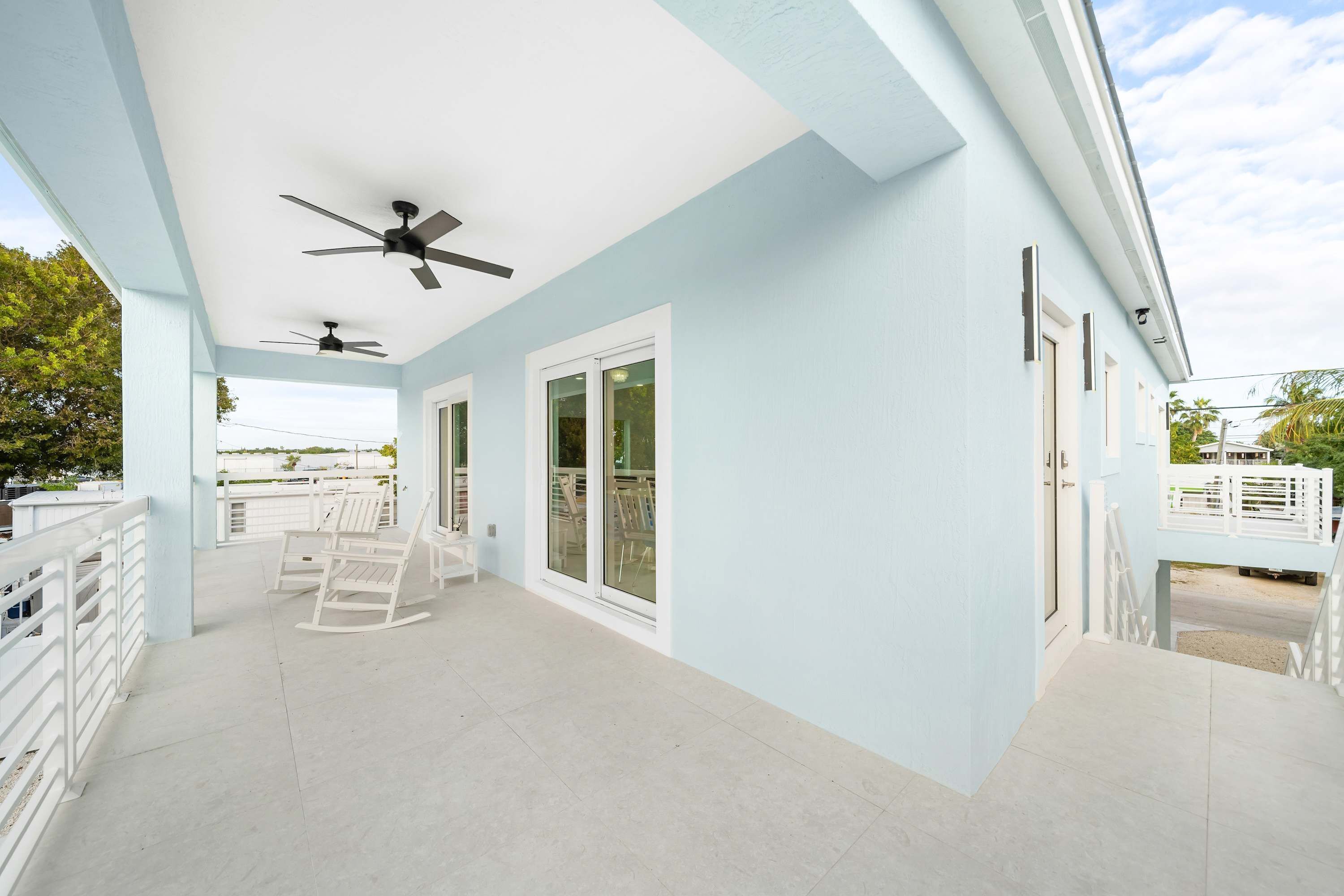 A covered patio area with ceiling fans, white rocking chairs, and a view of the surrounding landscape.