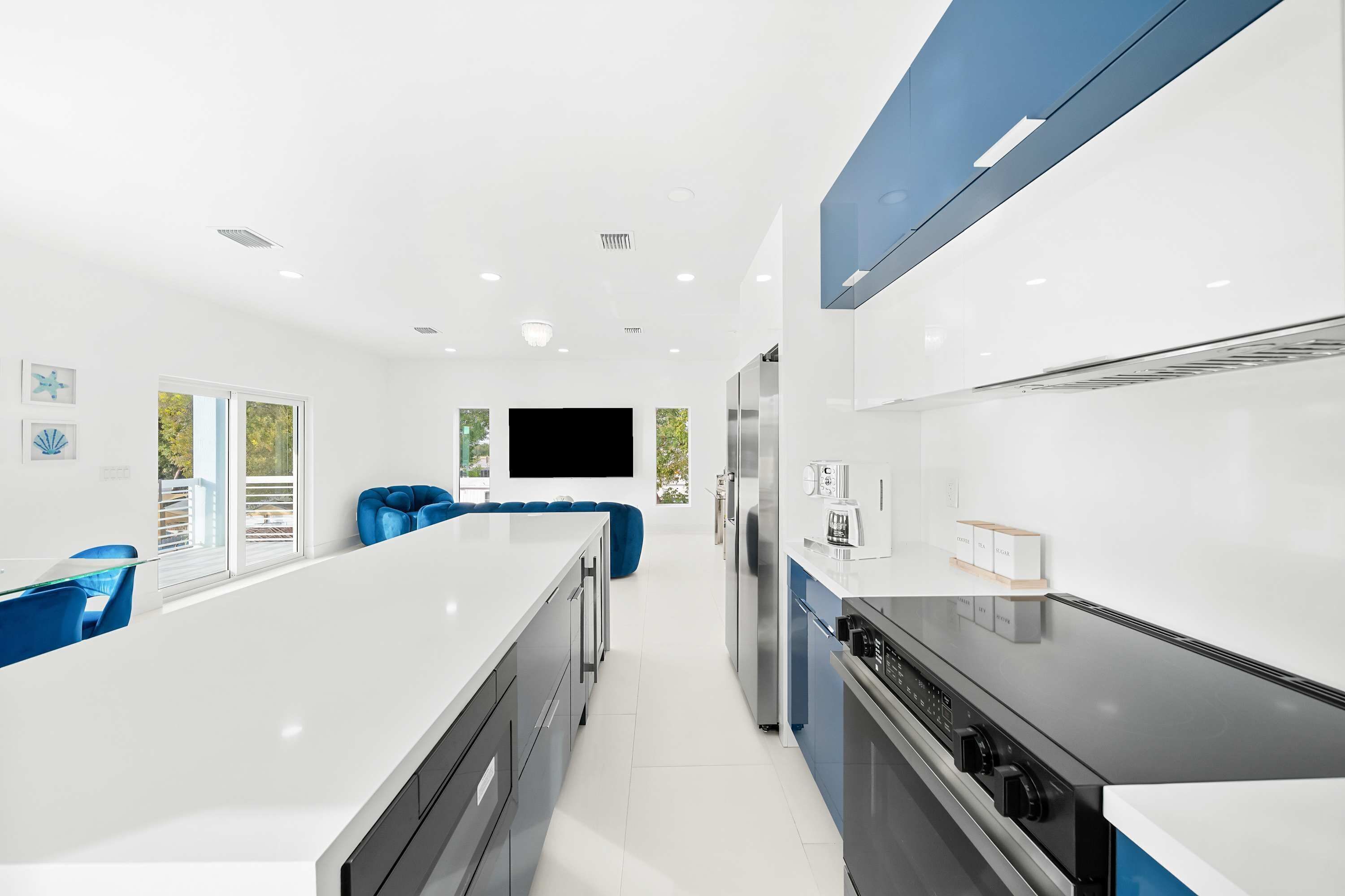 A modern kitchen with white countertops, a central island, and blue chairs.