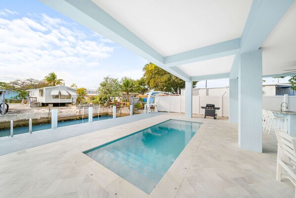 Un espace extérieur avec une piscine, un patio couvert, un petit bateau et un barbecue.