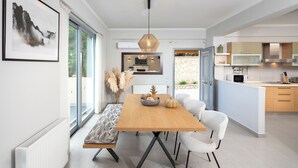 Une cuisine moderne avec une table à manger en bois, des chaises blanches et une vue sur l’extérieur.