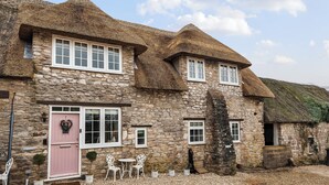 A stone building with a thatched roof, a pink door, and white-framed windows.