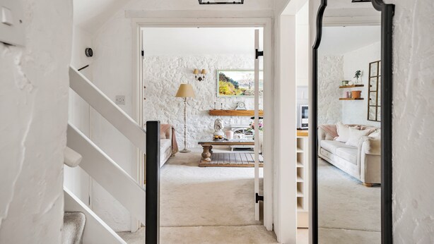 A hallway leading to a living room with a white staircase, a lamp, a table with a plant, and a sofa.