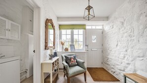 A well-lit room with a stone wall, a wooden chair with a cushion, a mirror, and a window with a green valance.