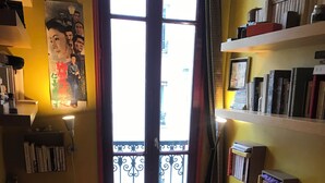 A bedroom with a bed, pillows, a window with a view, a bookshelf, and a wall-mounted lamp. - Charming apartment in Belleville (Paris)