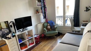 A living room with a sofa, a television, a chair, and a window with a view of the outside. - Charming apartment in Belleville (Paris)