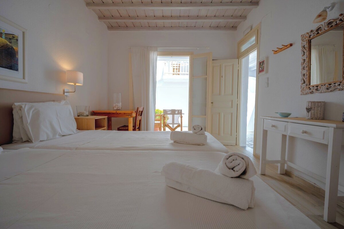 Une chambre d’hôtel avec deux lits, un bureau, une chaise et un balcon avec vue.