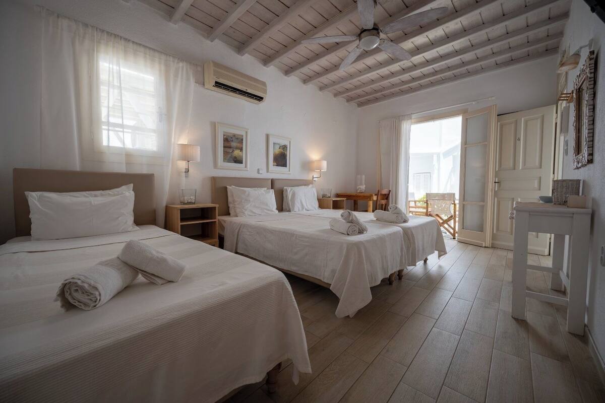 A hotel room with two beds, a ceiling fan, an air conditioning unit, a desk, and a chair.