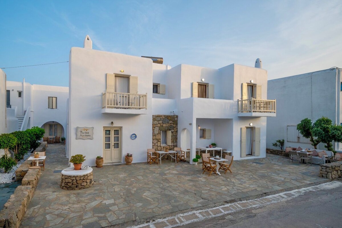 A white building with balconies, stone flooring, and outdoor seating areas.