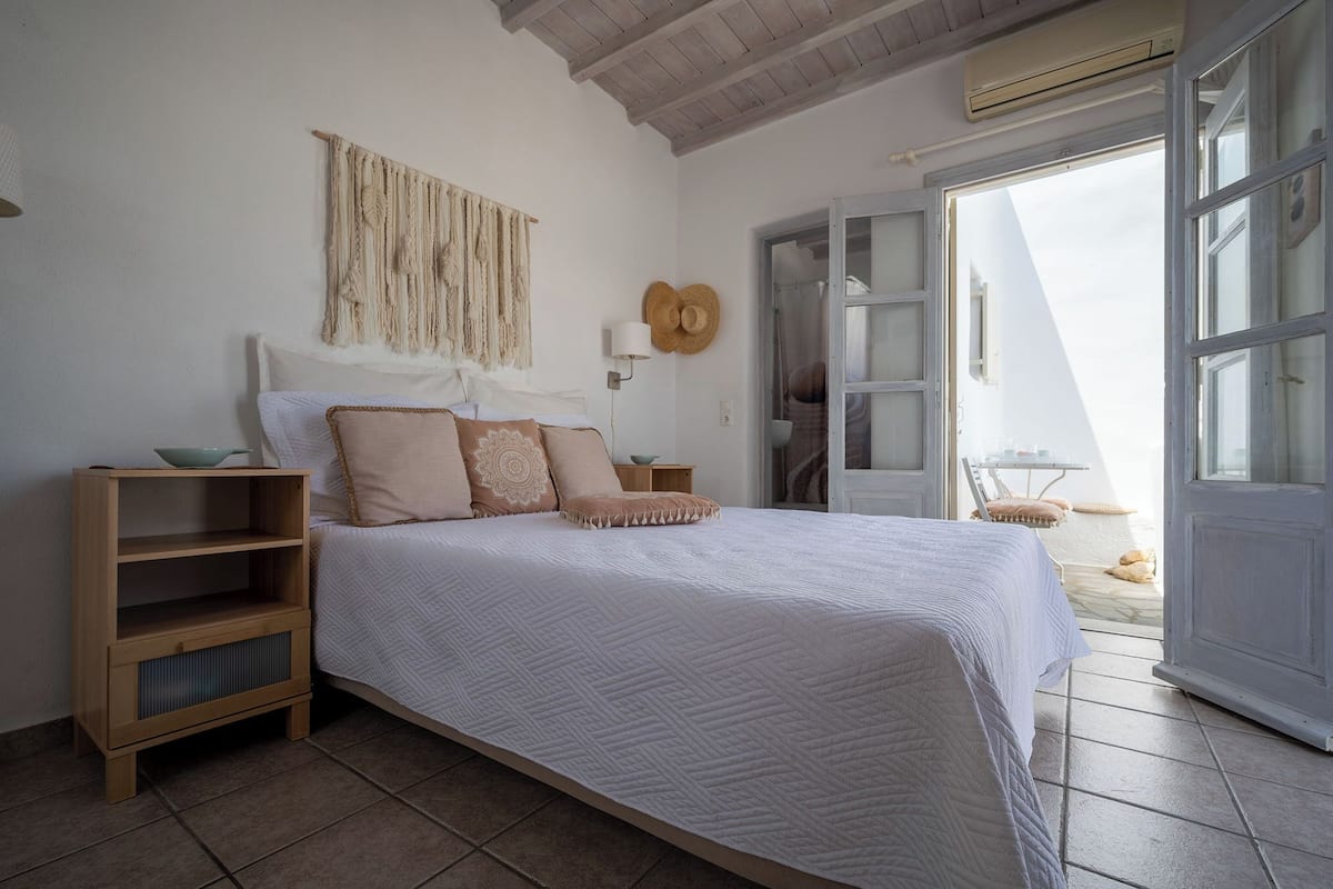 A bedroom with a bed, wooden nightstands, a macrame wall hanging, and a view through an open door.
