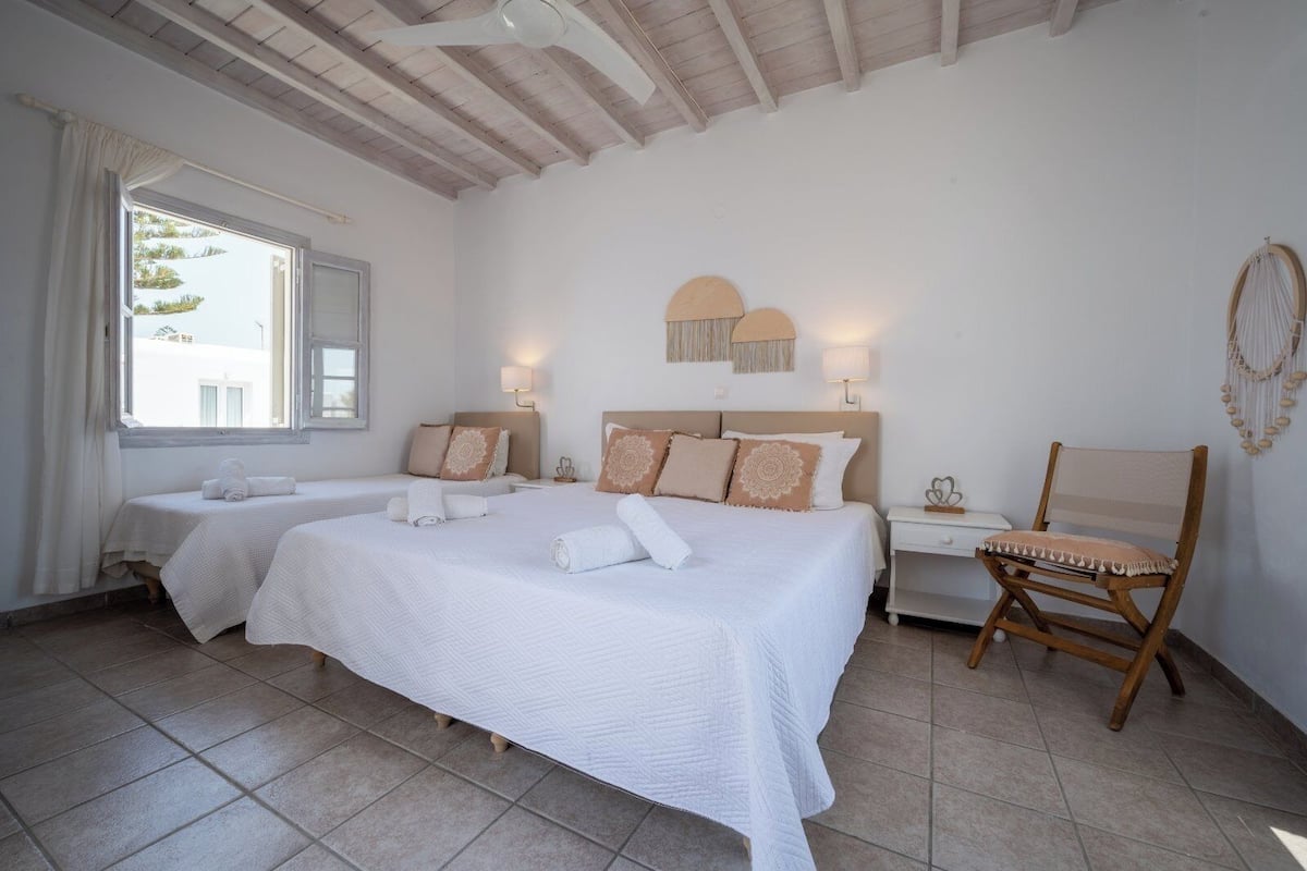 A hotel room with two beds, a wooden ceiling, a chair, and a window with curtains.