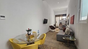 Un salon moderne avec une table à manger en verre, des chaises jaunes, un canapé gris et un téléviseur fixé au mur.