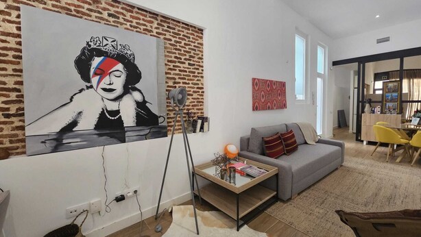 Un salon avec un grand tableau abstrait, un canapé gris, une table basse et un mur en briques.