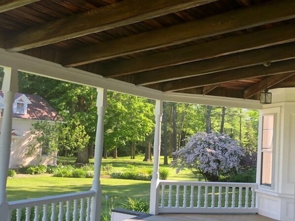 A covered porch with a view of a well-maintained garden and a house in the background.