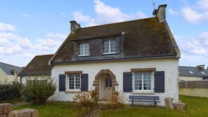 A two-story house with a stone foundation, a pitched roof, and a small front garden with a bench.