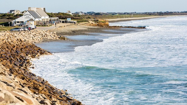 A coastal hotel with a rocky shoreline, a paved walkway, and a view of the sea.