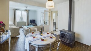 A cozy living room with a round dining table, a sofa, a TV, a fireplace, and a large window.