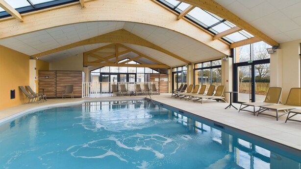 Ein Hallenbad mit hoher Decke und Dachfenstern, umgeben von Liegestühlen.