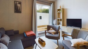 Ein modernes Wohnzimmer mit einer Couch, Sesseln, einem Couchtisch, einem Fernseher und einem Bücherregal.