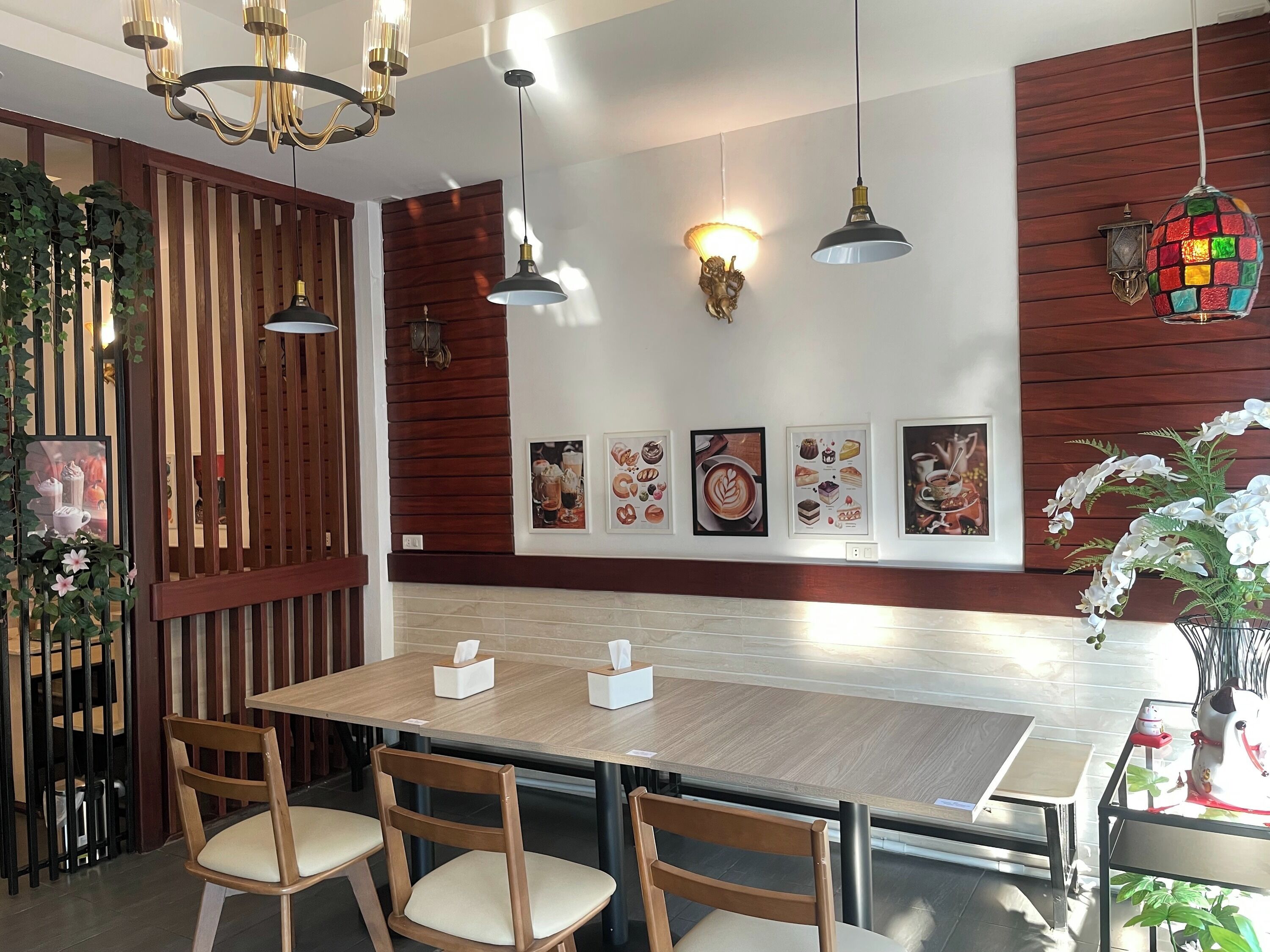 Un'area pranzo moderna con tavoli e sedie in legno, illuminazione a sospensione e opere d'arte appese al muro.