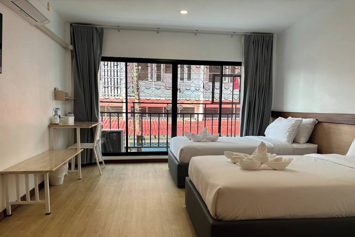 Une chambre d’hôtel avec deux lits, un bureau, une chaise et une grande fenêtre donnant sur un immeuble rouge.