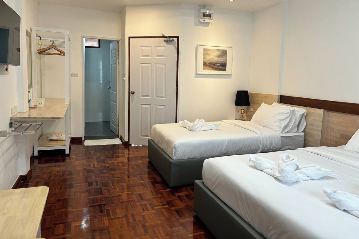 Une chambre d’hôtel avec deux lits, un bureau, une chaise, une armoire et un espace douche.