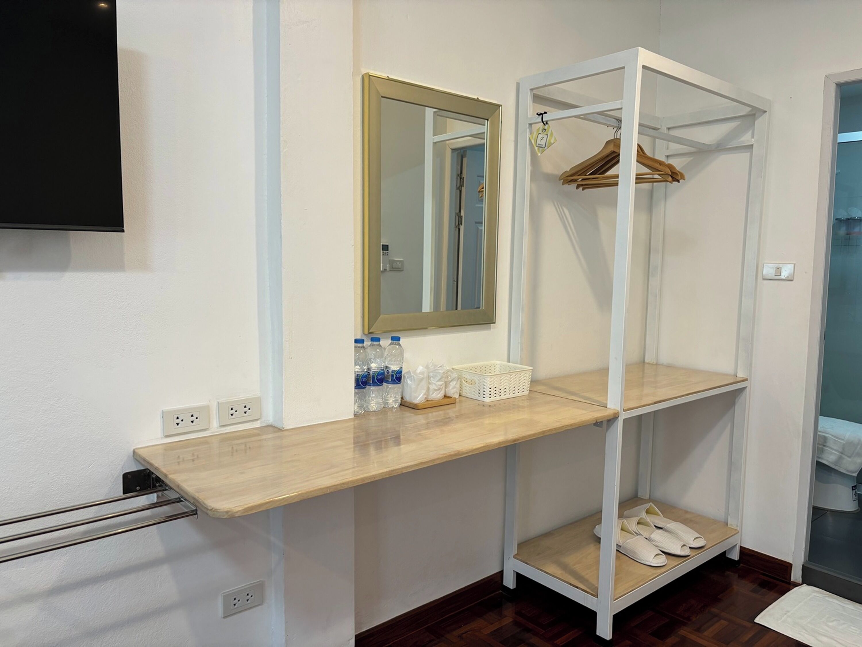 A bathroom with a wooden vanity, a mirror, a shelf with hanging clothes, and a towel rack.