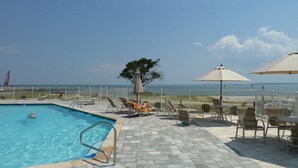 A swimming pool with a view of the ocean, surrounded by lounge chairs and umbrellas. - Artist Windmill Pt Condo Sunset Pool Relaxation (White Stone)