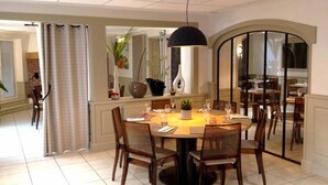 A dining area with a round table, chairs, a pendant light, and a glass partition. - Logis Hotel Restaurant Le Laurier Fleuri (Vertou)
