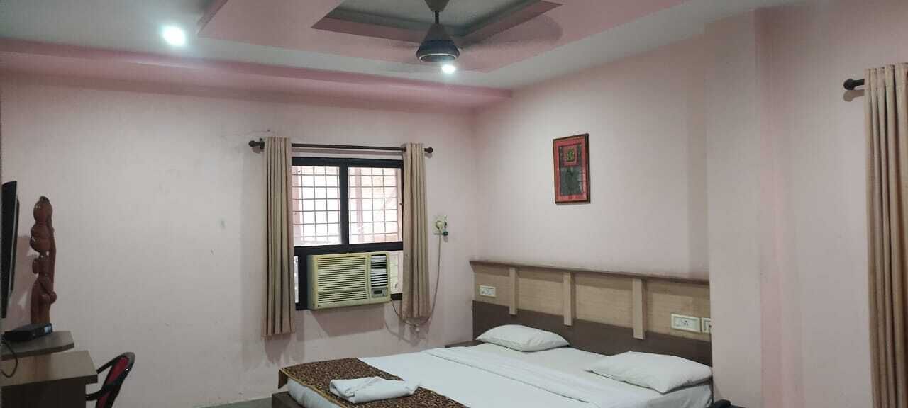 A bedroom with a bed, a window with curtains, an air conditioning unit, a ceiling fan, and a wall-mounted clock.