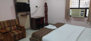 A hotel room with a bed, a sofa, a desk, a television, and an air conditioning unit. - Hotel Apsara Koraput (Jaypur)