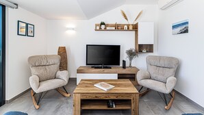 Un salon moderne doté d’un téléviseur à écran plat, de deux fauteuils à bascule, d’une table basse en bois et d’une bibliothèque agrémentée d’objets décoratifs.