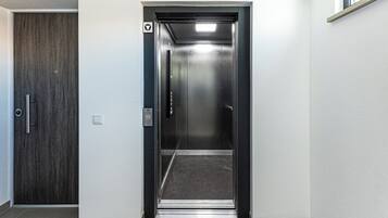 Un ascenseur avec un intérieur métallique, un panneau indiquant clairement la sortie de secours et une porte dotée d’une poignée.