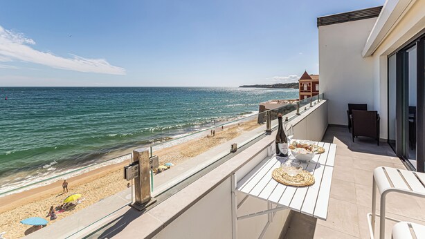 Un balcon avec vue sur la plage et l’océan, une table à manger avec de la nourriture et une chaise.