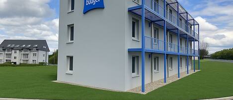 Un edificio moderno con un letrero que dice "ibis budget". Tiene techo plano, varias ventanas y una estructura metálica azul en el lateral.