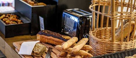 A variety of breads and pastries on a wooden table, a knife, and a toaster.