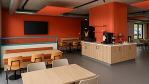 A modern cafe with a central island, seating area, and a large window. - Ibis Budget Auxerre Nord (Ouverture Printemps 2025) (Auxerre)