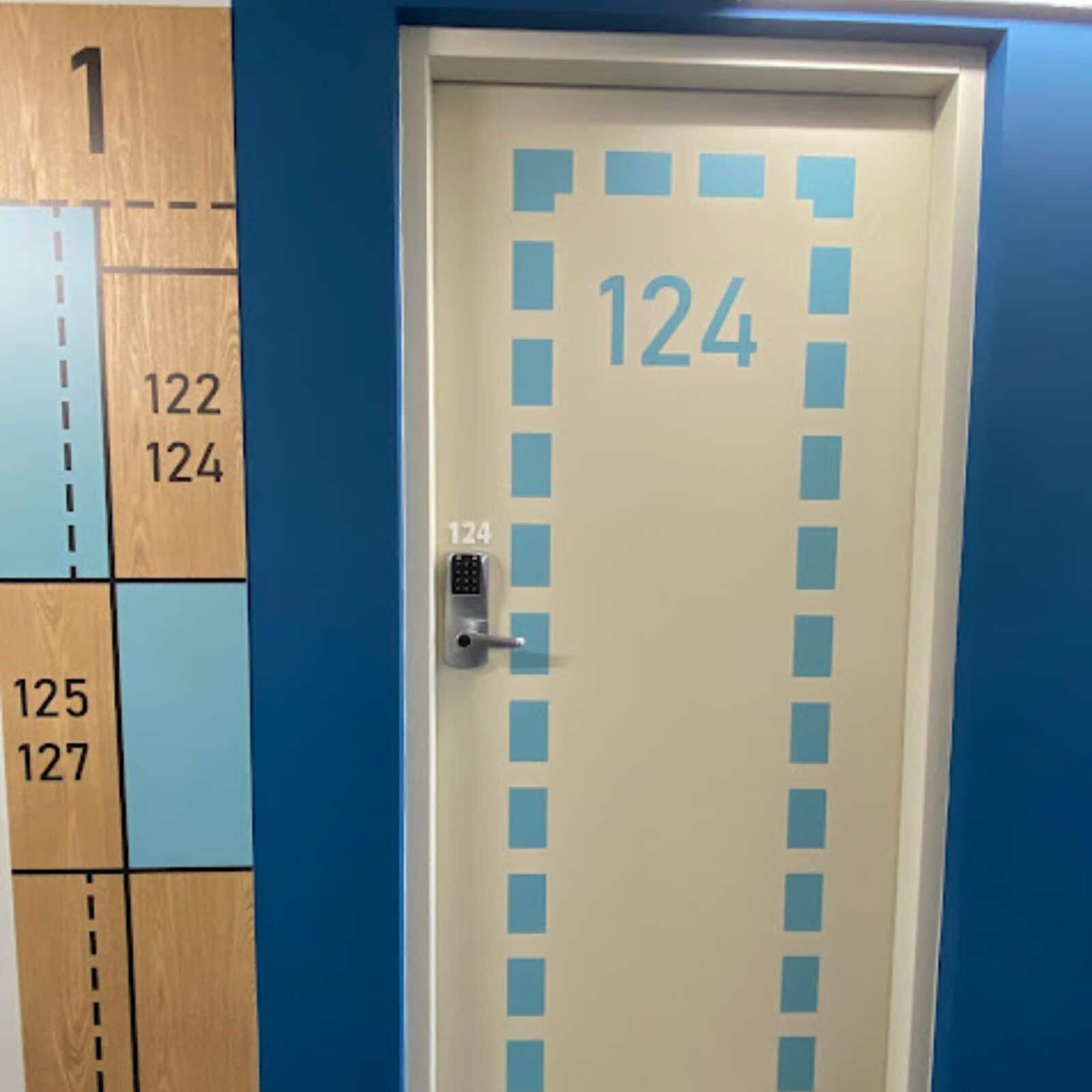 A hotel room door with the number 124, a keypad lock, and a blue wall with a number sequence from 1 to 127.