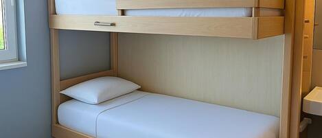A bunk bed with a wooden frame and white bedding in a room with light-colored walls and flooring.