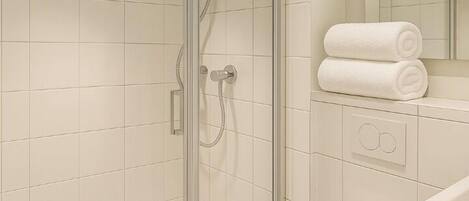 A modern bathroom with a glass-enclosed shower, white tiles, and a toilet.