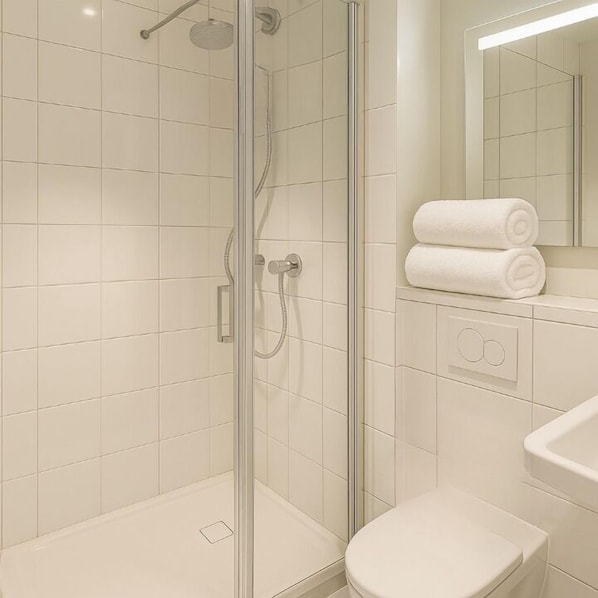 Uma casa de banho moderna com chuveiro de vidro, azulejos brancos e sanita.