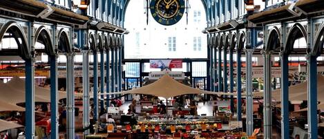 Un mercato al coperto con un orologio centrale, bancarelle e un soffitto alto con archi.