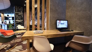 A modern reception area with a wooden desk, computer, and seating. - Ibis Budget Dijon Centre Clemenceau (Dijon)